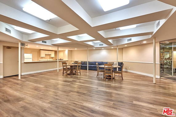 Indoor clubhouse area with wooden flooring, tables, chairs, and a kitchenette.