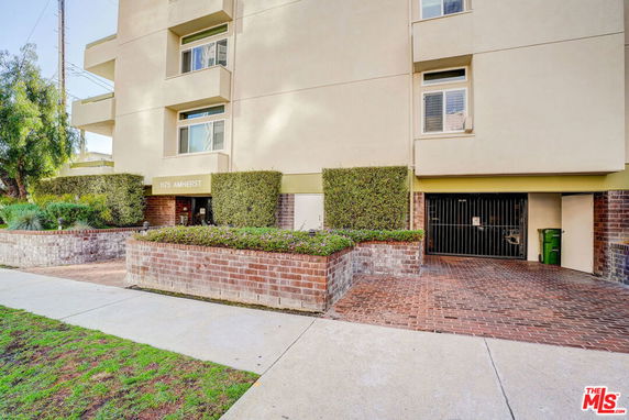 Front view of a multi-story building with brick and shrub landscaping.
