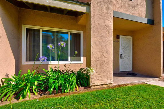 Front view of a house entrance with a large window and flowers in the garden.