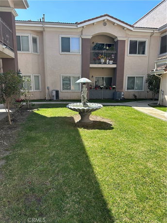 Front view of a two-story residential building with a central balcony and surrounding grass area.