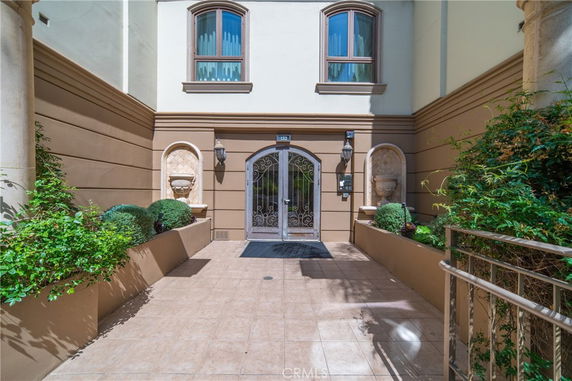 Front view of a building entrance with decorative landscaping and a wrought iron gate.