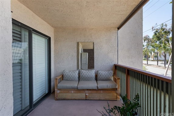 A balcony with a wooden bench, adjacent to a sliding glass door, offering a partial view of the street and trees beyond.