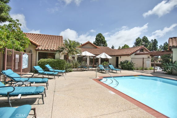 Outdoor swimming pool area with lounging chairs and umbrellas in front of a building with red-tiled roof.