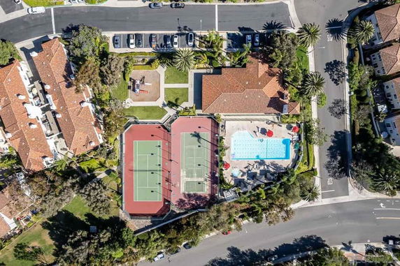 Aerial view of an outdoor area featuring tennis courts next to a swimming pool surrounded by buildings.