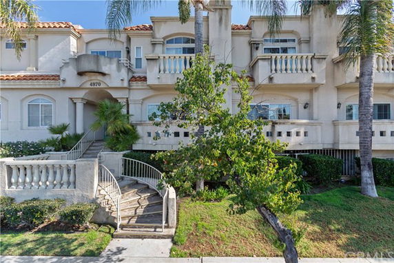 Front view of a multi-story residential building with balconies and a staircase leading to the entrance.