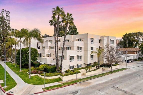 Front view of a multi-story residential building with balconies and palm trees.