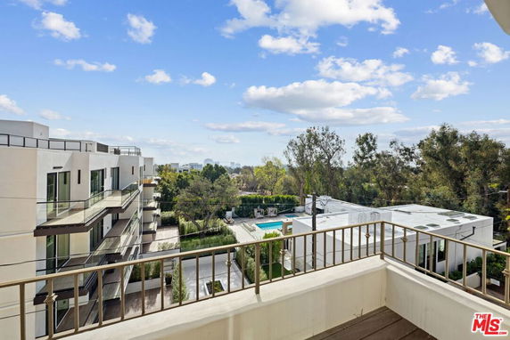 View from a balcony overlooking a residential building with trees and a swimming pool.