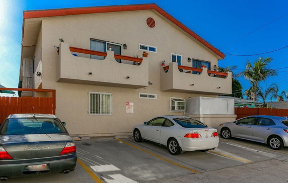 View of a building with a parking area in front, featuring cars parked in designated spaces.