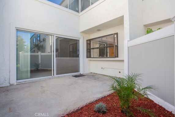 Exterior view of a building with glass sliding doors and a window, leading to a concrete patio area.