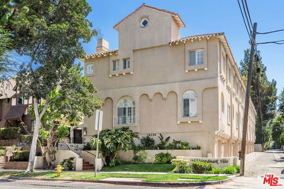 Front view of a multi-story residential building with arched windows and a small garden area.