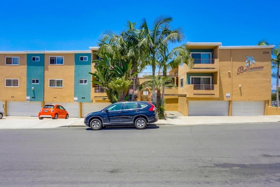 Front view of a multi-story apartment building with garages and palm trees.