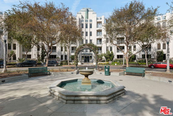 Front view of a multi-story building with a fountain and trees in the foreground.