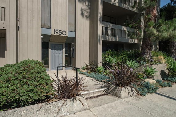Front view of a multi-story building with plants and a walkway.