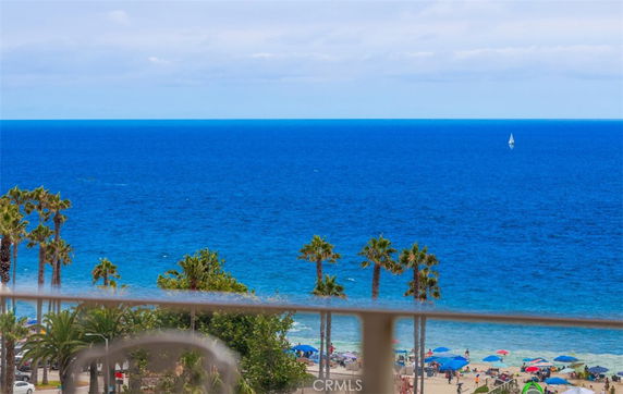 Wide angle view of the ocean and beach with palm trees, umbrellas, and a sailboat in the distance.