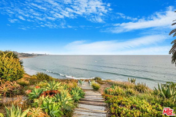 Panoramic view of the ocean with a path leading down through lush vegetation.