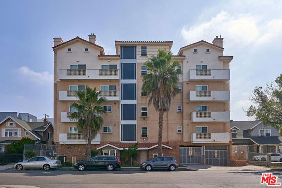 Front view of a multi-story apartment building with balconies and a central elevator shaft.