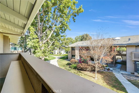 View from a balcony overlooking a residential area with pathways, trees, and neighboring buildings.
