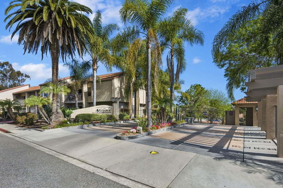 Front view of a residential complex with palm trees and a gated entrance.