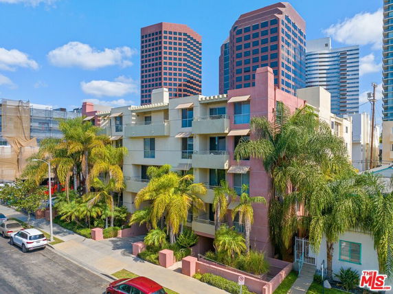 Front view of a multi-story residential building with balconies and surrounding palm trees.