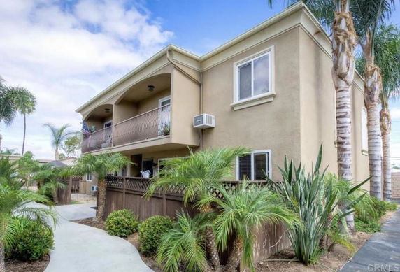 Front view of a two-story house with a balcony and surrounding greenery.