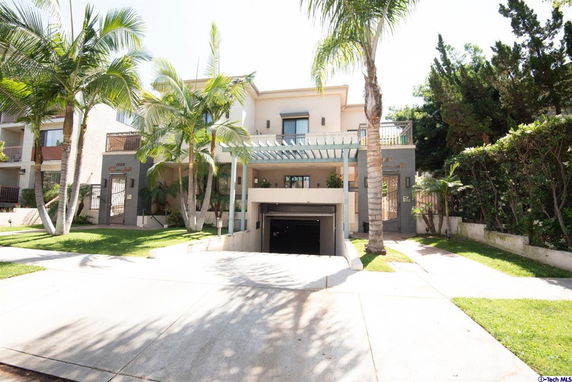 Front view of a multi-story building with palm trees and a garage entrance.