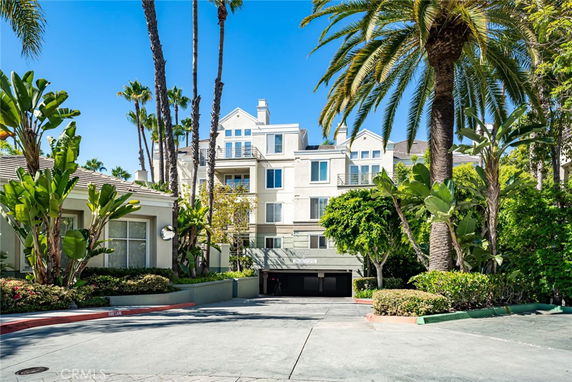 Front view of a multi-story building with balconies surrounded by palm trees.
