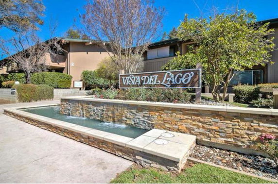 Front view of a building complex with a sign 'VISTA DEL LAGO' and a decorative stone water feature.