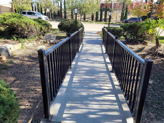 Pathway with metal railings leading through a landscaped area with greenery and trees.