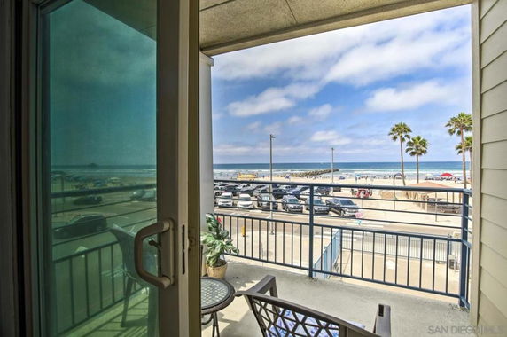 View from a balcony overlooking a beach with palm trees and parked cars.