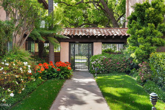 Front view of a house with a tiled roof and gated entrance surrounded by lush greenery and flowers.