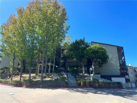 Front view of a multi-story residential building with balconies and surrounding trees.