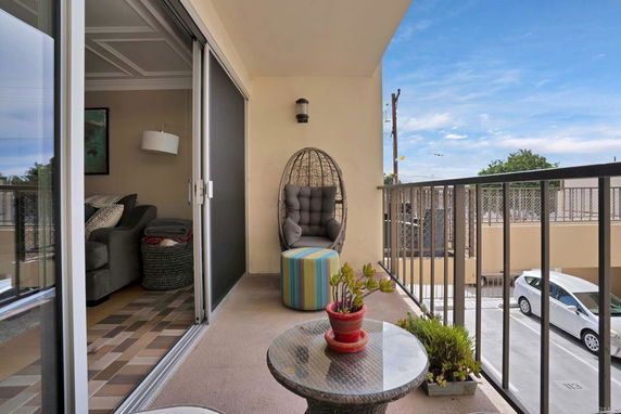 View from a balcony with a chair and table, overlooking a parking area.