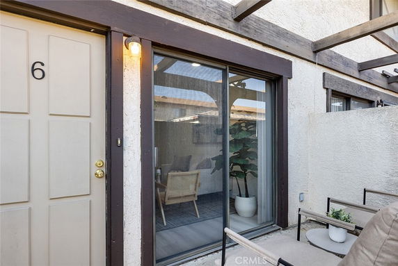 Front view of a building entrance with a door marked number 6, sliding glass window, and outdoor sitting area.