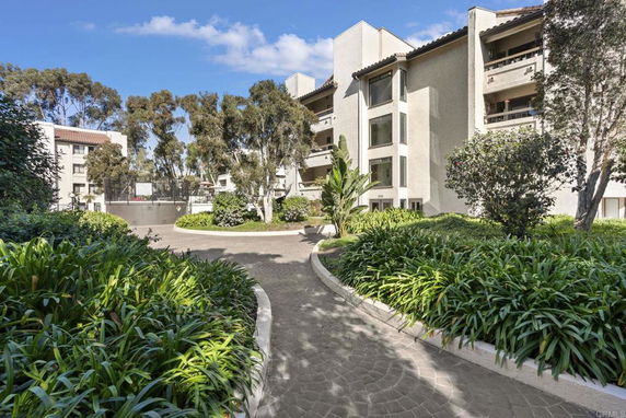 Front view of a multi-story apartment complex with balconies and surrounding greenery.