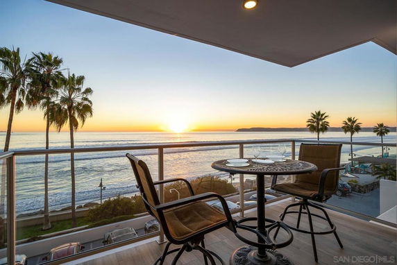Panoramic view of the ocean and palm trees from a balcony with outdoor seating.
