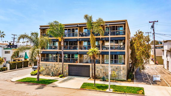 Front view of a multi-story apartment building with balconies and palm trees.