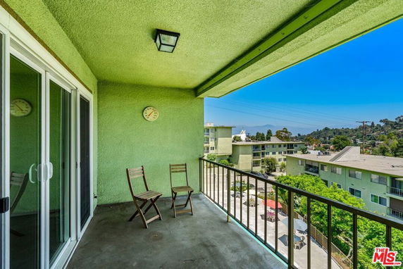 Balcony view from an apartment with green walls and two chairs overlooking surrounding buildings and landscape.