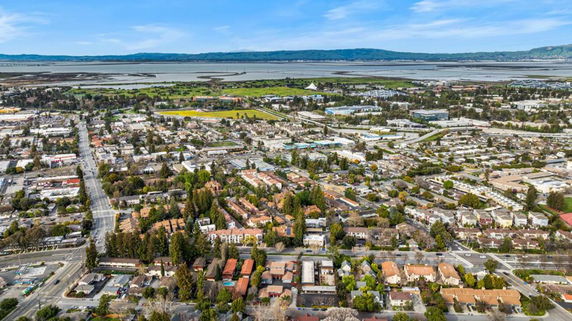 Aerial view of a cityscape with houses, buildings, roads, and a body of water in the background.