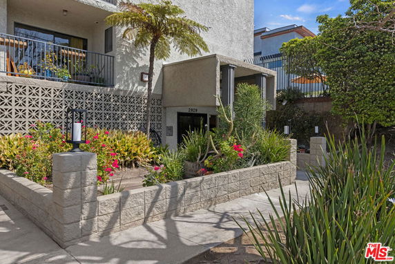 Front view of a multi-story building with a balcony and landscaped garden.