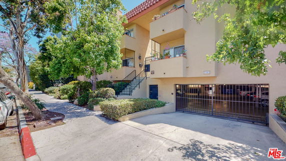 Front view of a multi-story residential building with balconies and a gated parking area.