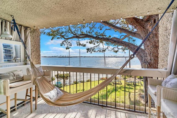 View from a balcony with a hammock overlooking a body of water and a tree.