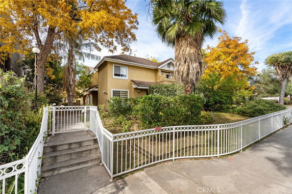 Front view of a two-story house with a white fence and trees.