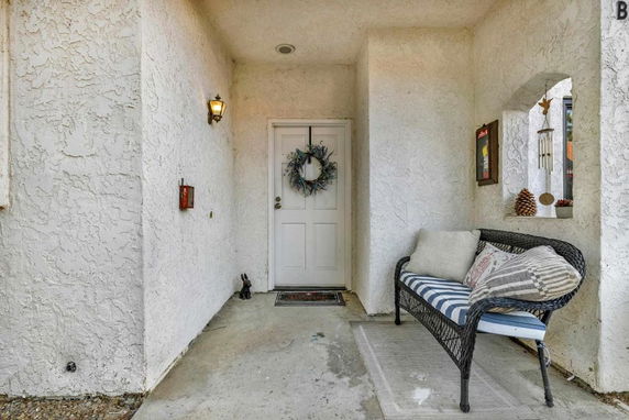 Front entrance of a house with a white door and a decorative wreath, accompanied by a wicker bench with cushions on a small porch.