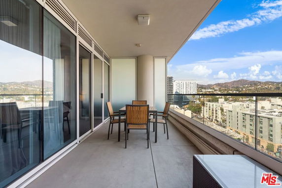 Outdoor balcony with glass railing offering a panoramic view of the cityscape and hills.