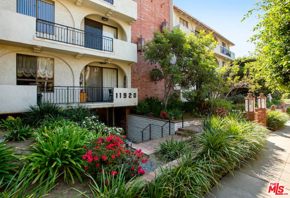 Front view of a multi-story residential building with balconies and surrounding greenery.