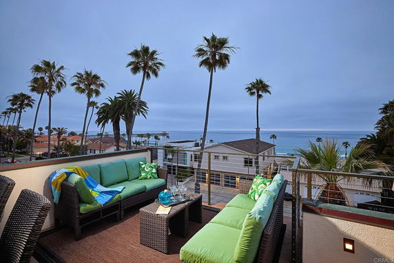 Outdoor seating area with a view of the ocean and palm trees in the distance.
