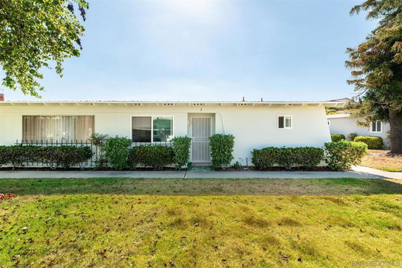 Front view of a single-story house with a flat roof and surrounding shrubbery.