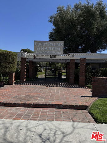 Front view of an entrance to a condominium complex with brick pillars and a sign reading 'Coco Palms Anaheim Condominiums.'
