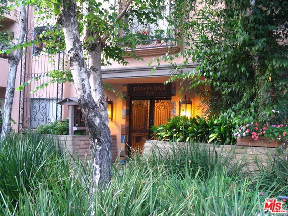 Front view of a building entrance with decorative lighting and lush greenery.