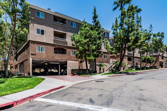 Front view of a multi-story apartment building with open parking on the ground level.